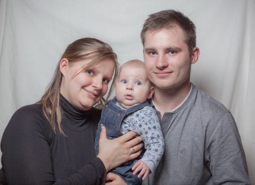 Ein Paar hält gemeinsam ihr Baby im Arm und blickt in die Kamera.