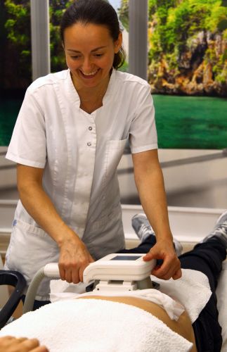 Eine Frau in weißer Arbeitskleidung führt eine Kryolipolyse-Behandlung an einer liegenden Person durch.