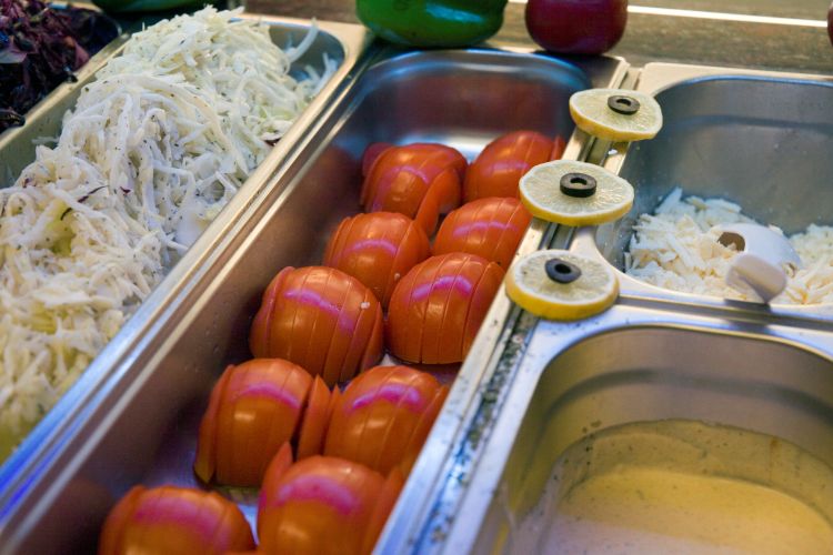 Metallbehälter mit frischen Zutaten wie Kohl, Tomaten, Zitronenscheiben, Käse und Dressing in dem Dönerladen